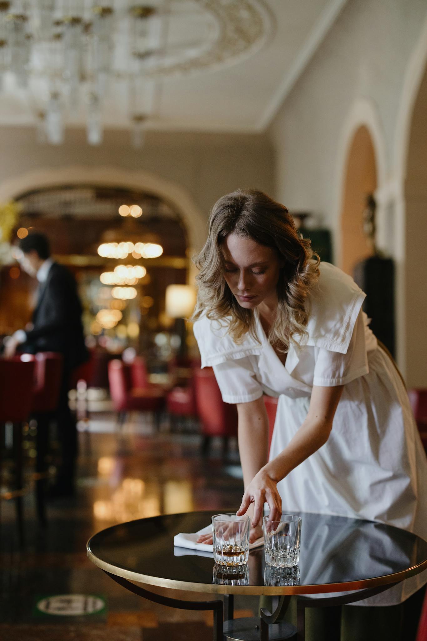Elegant waitress cleaning a table in a luxurious restaurant interior with warm lighting.